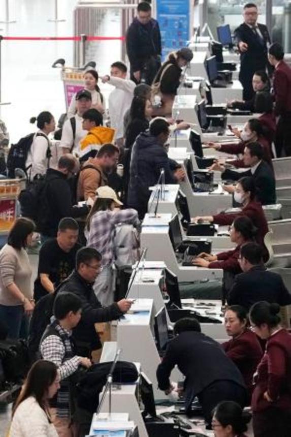 　北京首都空港の日本便などを扱うカウンターで搭乗手続きをする人たち＝１５日（共同）