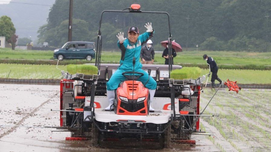 田植え機の上でポーズを取る三山ひろしさん＝山県市岩佐