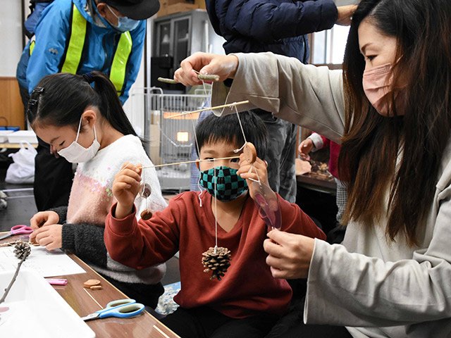 松ぼっくりや木で飾りを作る親子＝同市赤保木町