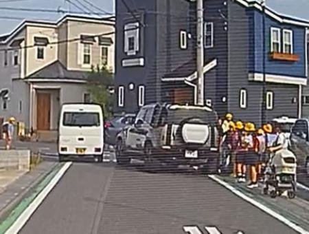 　埼玉県三郷市の市道で、小学生らの脇に止まった車（右）＝１４日（住民提供）