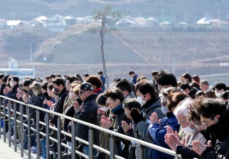 　東日本大震災から１５年、地震発生時刻に合わせて黙とうする人たち。奥は「奇跡の一本松」＝１１日午後２時４６分、岩手県陸前高田市の高田松原津波復興祈念公園