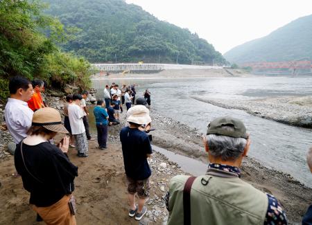 　２０２０年７月の豪雨から５年となり、氾濫で多くの被害をもたらした球磨川（奥）周辺で黙とうする人たち＝４日午前、熊本県八代市