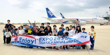 　万博を記念した全日空の特別デザイン機を前に記念撮影する小学生ら＝１９日午後、能登空港
