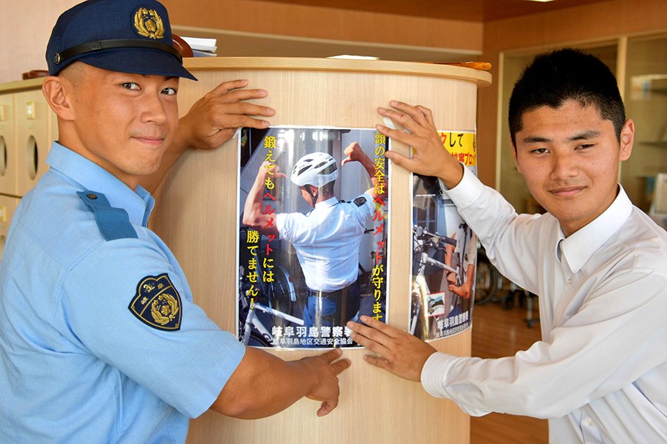 ヘルメット着用啓発ポスターを貼る山田勇志巡査長（左）ら＝羽島市正木町大浦、羽島特別支援学校