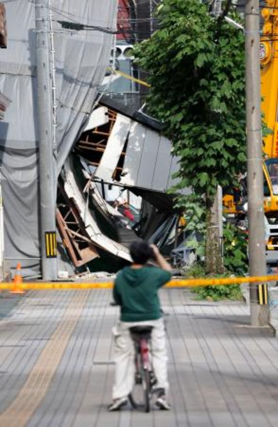 　解体工事中の建物が倒壊した現場（奥）＝１５日午後４時３２分、福岡県久留米市