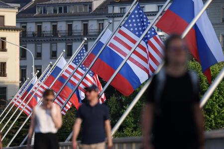 　街に掲げられた米国とロシアの国旗の下を歩く人々＝２０２１年、ジュネーブ（ゲッティ＝共同）