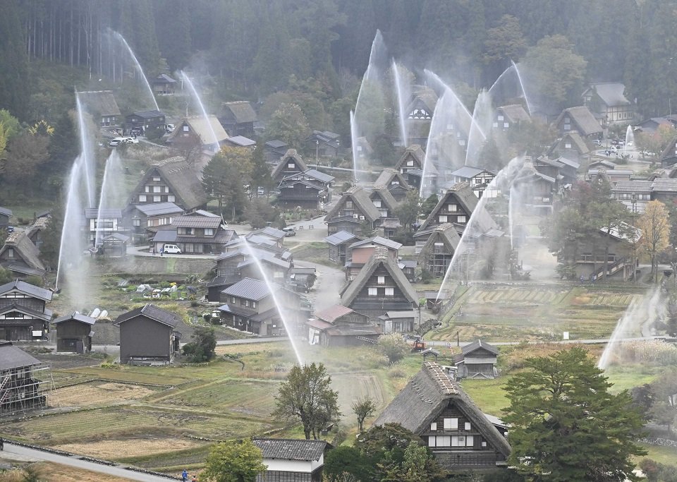 放水訓練で合掌造り集落に高々と上がる水柱＝３０日午前８時２分、大野郡白川村荻町