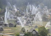 放水訓練で合掌造り集落に高々と上がる水柱＝３０日午前８時２分、大野郡白川村荻町