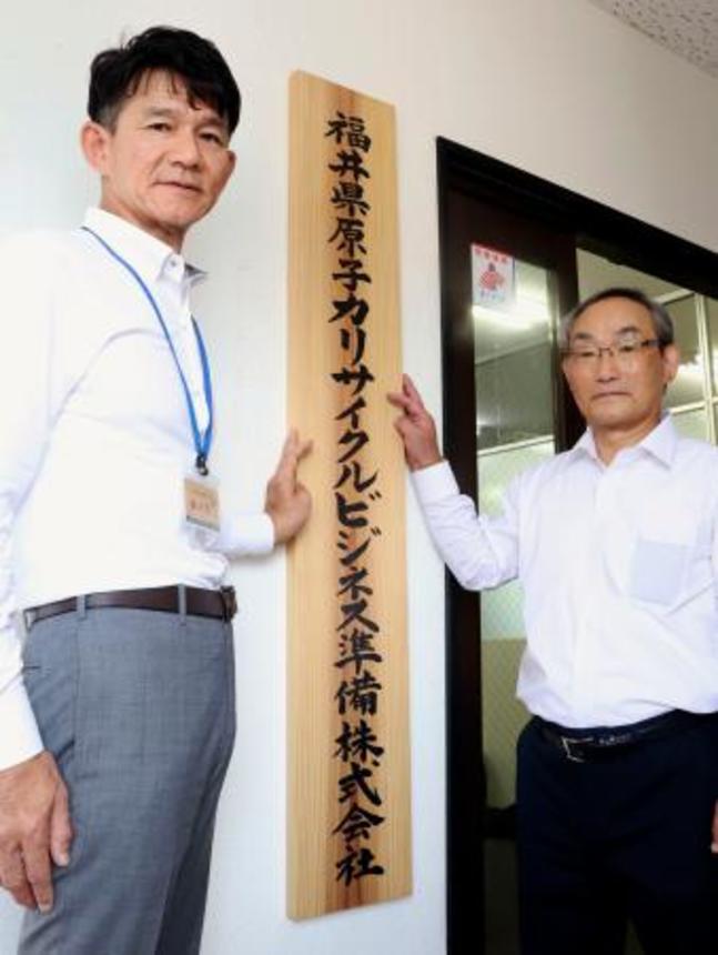 　福井県原子力リサイクルビジネス準備株式会社の事務所入り口に看板を設置する来馬克美社長（右）ら＝１日午前、福井県敦賀市