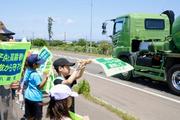 　事故現場付近で走行車両に向かって旗を振り、安全を呼びかける小学生ら＝１８日午前、北海道八雲町