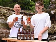 倒れた大杉の前で完成したビールを手にする田村啓さんと東恵理子社長（右）＝瑞浪市大湫町、大湫神明神社
