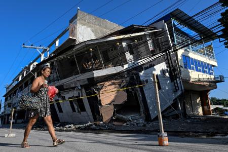 　フィリピンのミンダナオ島で、地震により倒壊した建物のそばを通り過ぎる女性＝９日、ジェネラルサントス（ロイター＝共同）