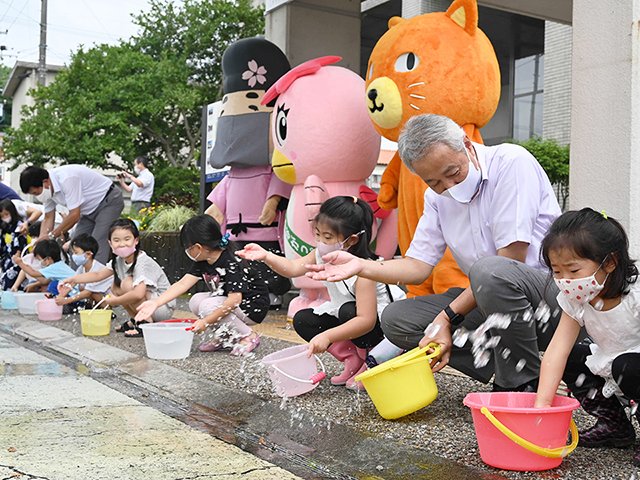 道路に手で水をまく子どもら＝多治見市役所