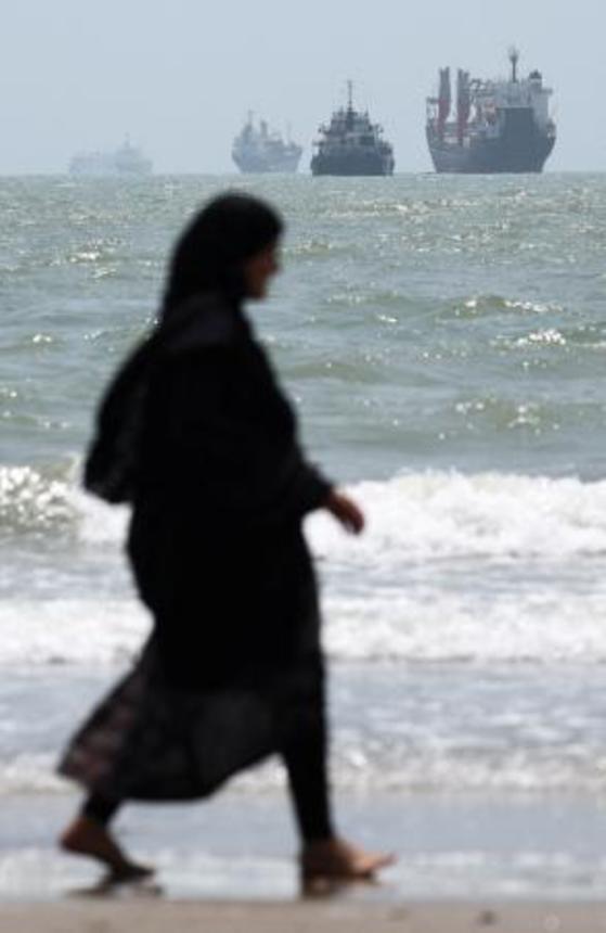 　ホルムズ海峡に臨む海岸を歩く女性。沖合には船舶が浮かんでいる＝２５日、イラン南部バンダルアバス（ＷＡＮＡ提供、ロイター＝共同）