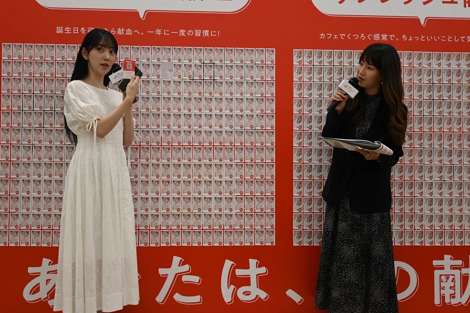 自身の写真を掲載したノベルティを紹介する堀未央奈さん（左）＝県庁