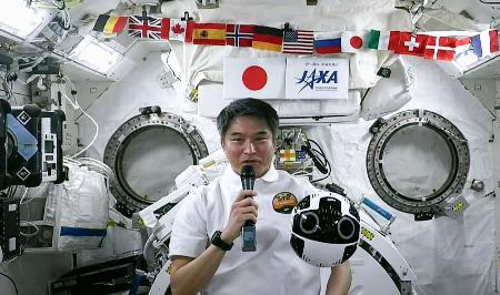 　２０日、国際宇宙ステーションで記者会見する大西卓哉飛行士。手前右に浮いているのは船内撮影用ロボット「イントボール２」（ＪＡＸＡの中継から）