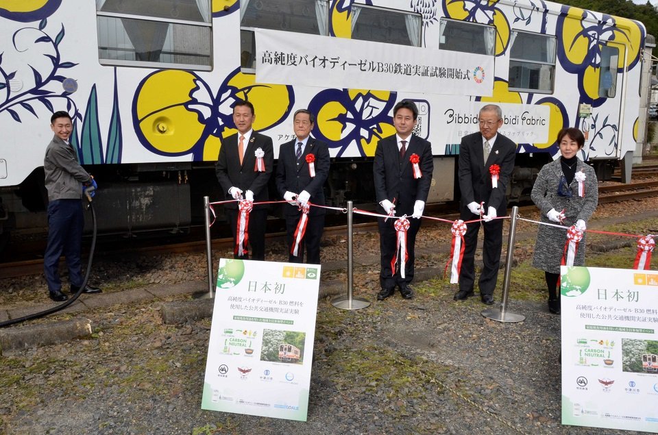  実証実験開始を記念して給油とテープカットをする関係者＝恵那市明智町、明智駅 