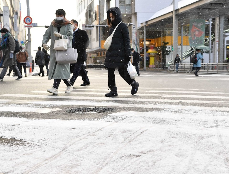 雪が舞う中を歩く人たち＝２５日午前８時５分、岐阜市神田町
