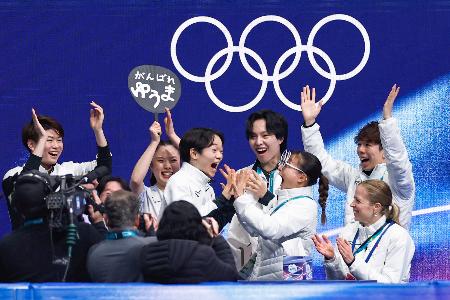 　団体男子ＳＰの得点を確認し、坂本花織（前列右から２人目）と手を合わせて喜ぶ鍵山優真＝ミラノ（共同）