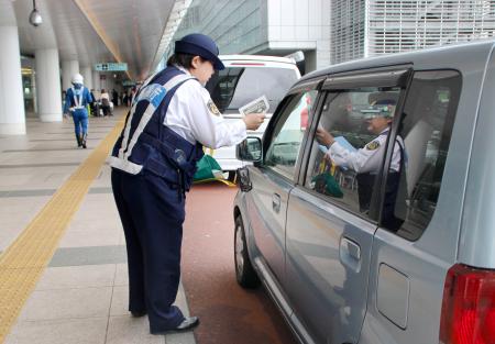 　羽田空港第３ターミナル前で、違法駐車禁止を呼びかけるチラシを配る警察官＝２５日午前