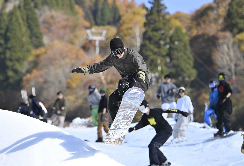 紅葉を背に初滑りを楽しむスノーボーダー＝３日午前１０時４２分、郡上市白鳥町石徹白、ウイングヒルズ白鳥リゾート