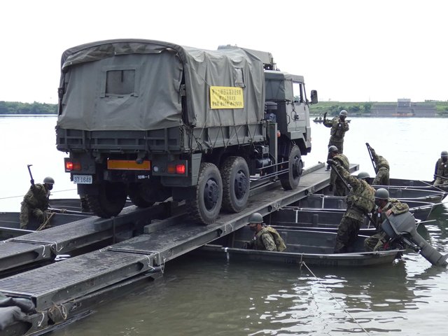渡河ボートを連結させた「軽門橋」で、陸自の大型トラックを木曽川に浮かべる隊員＝羽島市下中町城屋敷