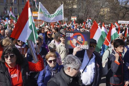 　ハンガリーの首都ブダペストで、ウクライナのゼレンスキー大統領らの顔写真と共に「戦争をやめろ」と記したプラカードを掲げて行進するフィデス支持者ら＝３月（共同）