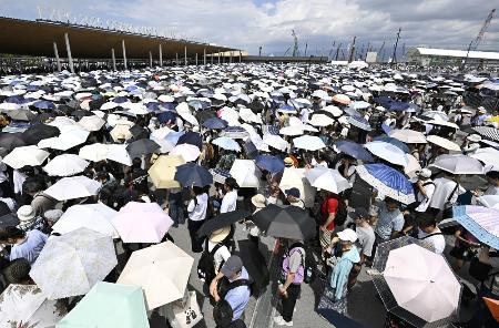 　強い日差しの中、日傘を差して大阪・関西万博の入場ゲートに並ぶ大勢の人たち。万博は１３日で開幕３カ月の折り返し＝１２日、大阪市此花区の夢洲