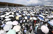 　強い日差しの中、日傘を差して大阪・関西万博の入場ゲートに並ぶ大勢の人たち。万博は１３日で開幕３カ月の折り返し＝１２日、大阪市此花区の夢洲