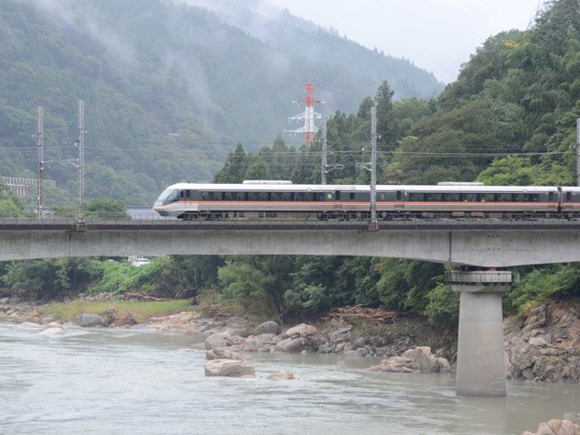 ３週間ぶりに運転を再開した特急「ワイドビューしなの」。長野方面に向かって大雨の爪痕が残る木曽川を渡る＝中津川市坂下