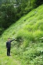 茅場でカリヤスを指さす白川村教育委員会の尾崎達也さん