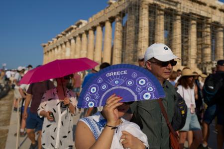 　アテネのパルテノン神殿前で、扇子や傘で日差しを遮る観光客ら＝７月（ＡＰ＝共同）