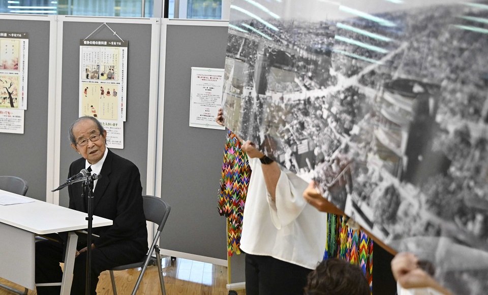 式典で焼け跡の写真を解説する岐阜空襲を記録する会の篠崎喜樹代表＝９日午前１０時８分、岐阜市役所