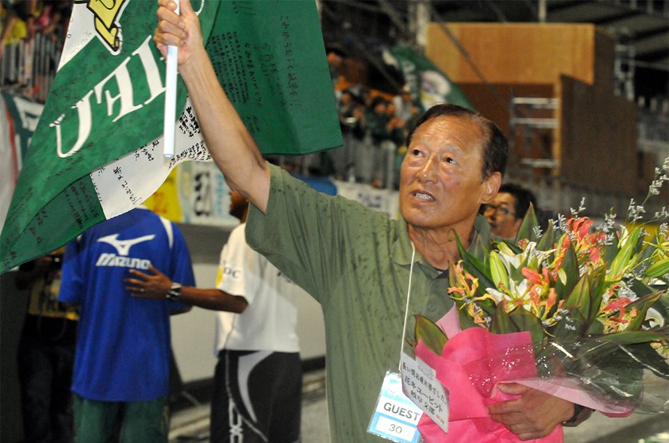 社長を退任し、サポーターからの寄せ書きが書き込まれたフラッグを手にあいさつする今西和男さん＝２０１２年、長良川競技場