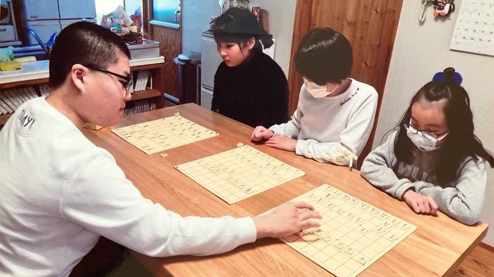 岩佐美帆子現女流１級（右から３人目）ら生徒たちと将棋を指す高校２年生の頃の高田明浩さん＝２０２０年１月、各務原市鵜沼朝日町、文聞分