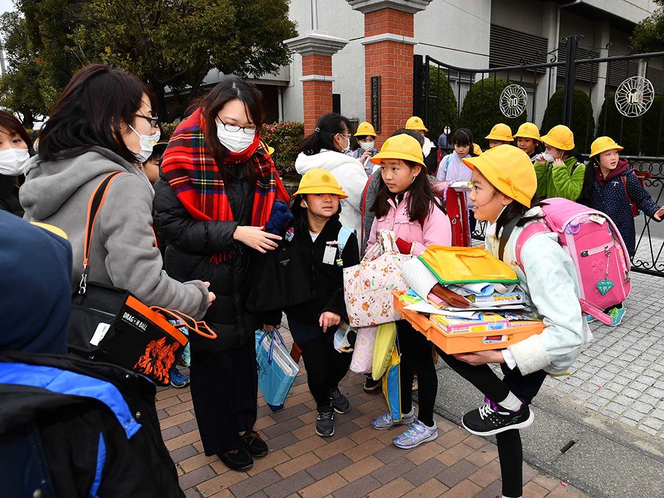 臨時休校が決まり、本年度最後の授業の日となった２８日。ランドセル姿を見に、学校まで迎えに来た母親と話す小学６年の児童ら＝午後４時１８分、岐阜市加納西丸町、加納小学校