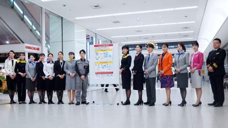 　モバイルバッテリーの取り扱い変更を周知するポスターと航空各社の社員ら＝１４日午後、羽田空港