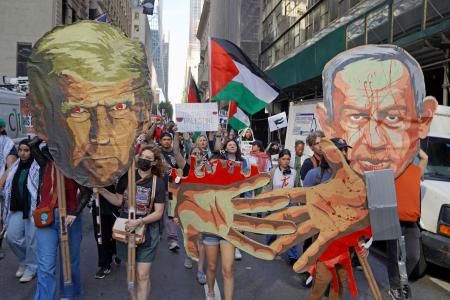 　２６日、米ニューヨークで行われた抗議デモ。トランプ大統領とネタニヤフ首相の似顔絵や、血塗られた手のイラストを持って歩く参加者もいた（共同）