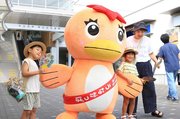 熱中症対策を呼び掛けるため、ＪＲ多治見駅で家族連れにうちわを配る市公式キャラクター「うながっぱ」＝８月、多治見市白山町