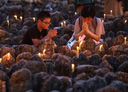 　化野念仏寺で始まった「千灯供養」で、石仏に手を合わせる参拝者ら＝３０日夕、京都市右京区