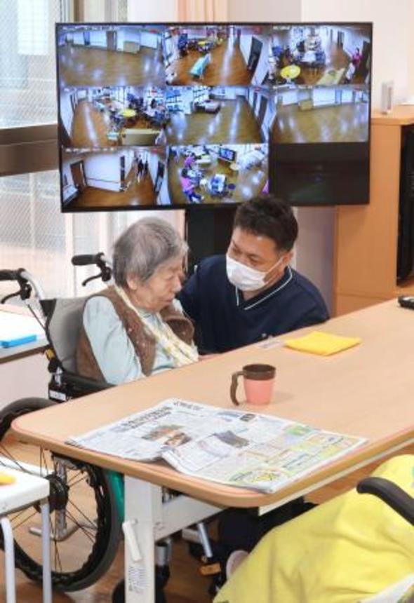 　能登半島地震で被災した介護施設で、利用者（左）と話す職員。テレビには施設内の各所の様子が映っていた＝２９日午前、石川県輪島市