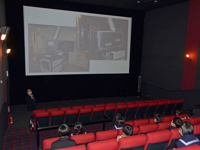 劇場内で磯谷貴彦さんから映画館の業務について説明を受ける生徒＝関市倉知、シネックスマーゴ