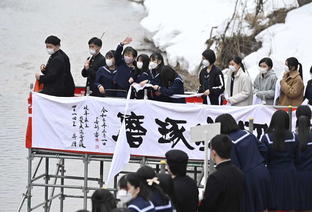 雪の残る川べりの足場からスカーフを流す卒業生たち＝１日午後０時２８分、岐阜県高山市大新町、大八賀川