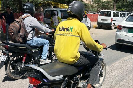 　インド・ニューデリーの路上をバイクで走る「ブリンキット」の配達員（手前）＝１３日（共同）