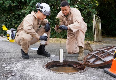 　白い泡が出ているのが見つかったマンホールを調査する米軍関係者＝２９日午後、沖縄県宜野湾市