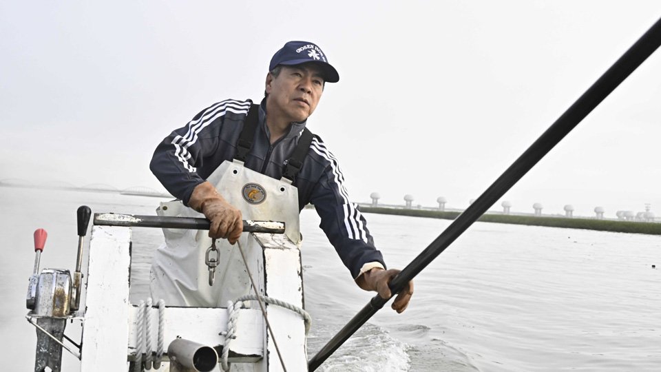 ヤマトシジミを取る水谷隆行組合長。堤の向こうに長良川河口堰が見えた＝１５日、三重県桑名市、揖斐川