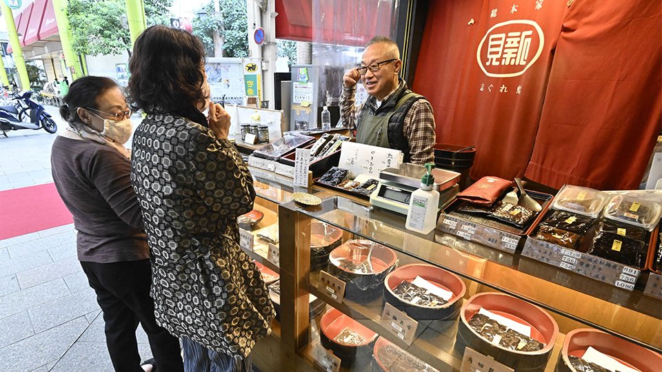 貝のしぐれ煮や昆布のつくだ煮が並ぶ店に立つ佐合達朗さん（中央）＝１６日、岐阜市日ノ出町、岐阜貝新日ノ出町店