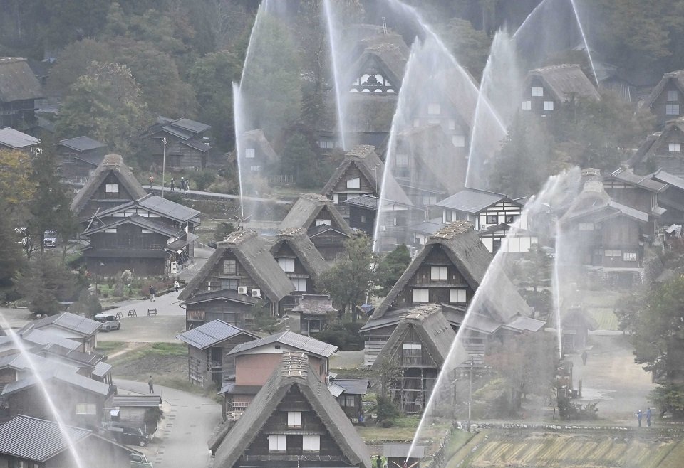 放水訓練で合掌造り集落に高々と上がる水柱＝３０日午前８時２分、大野郡白川村荻町