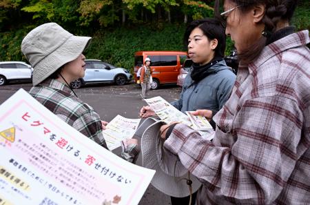 　登山客にヒグマへの注意を呼びかけるチラシを配るＮＰＯのボランティア（右から２人目）＝１０月、札幌市