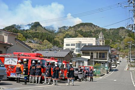 　避難所となっている吉里吉里学園小学部（奥）近くから立ち上る煙＝２４日午前、岩手県大槌町